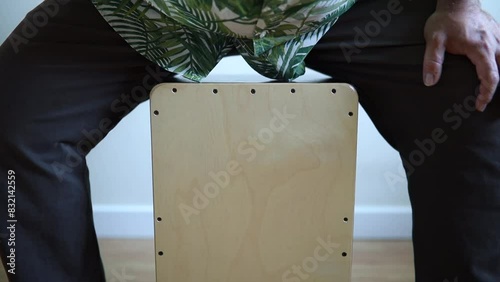 unrecognizable musician plays with his hands on a cajon flamenco while sitting on it. 