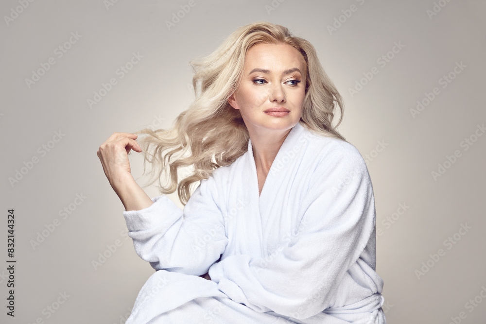 Beautiful dreaming mature blonde woman having clean skin in housecoat over a grey isolated background. Beautiful dreaming mature blonde woman having clean skin in housecoat over a grey isolated background.