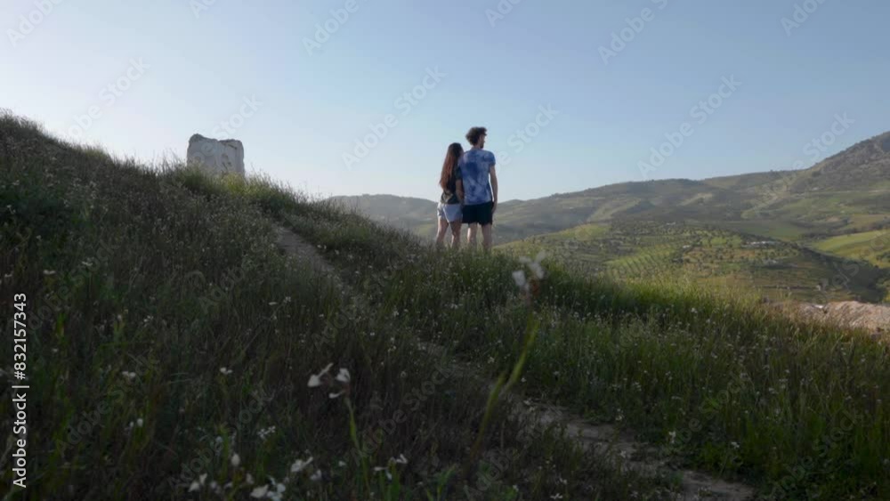 Couple looks out across rolling grass hills of Fez Morocco with wildflowers off path Couple looks out across rolling grass hills of Fez Morocco with wildflowers off path