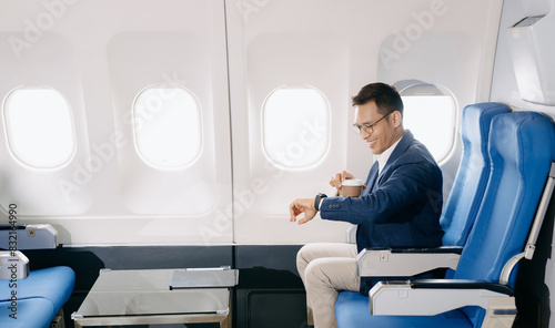 Attractive Asian male passenger of airplane sitting in comfortable seat while working laptop and tablet with mock up area using wireless connection.