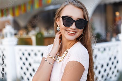 Happy beautiful young woman with a smile with fashion sunglasses in a fashionable dress walking and having fun in the city