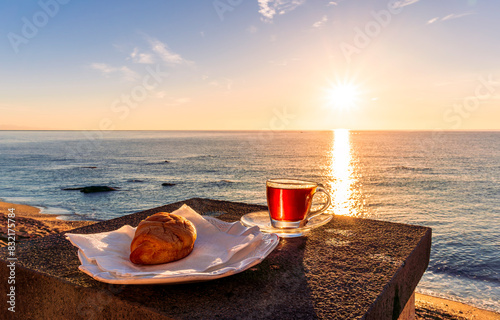 concept of street outdoor breakfast with a cup of tea or coffee on a morning coast during sunrise. landscape of city embarkment with sea water and cloudy sky on background