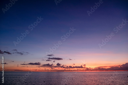 A tranquil seascape at sunset with vibrant orange and purple hues painting the sky and gentle waves on the water surface. photo
