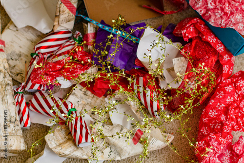 A cluttered arrangement of colorful Christmas gift wrapping paper, ribbons, and bows scattered on the floor, indicating a recent unwrapping session. photo