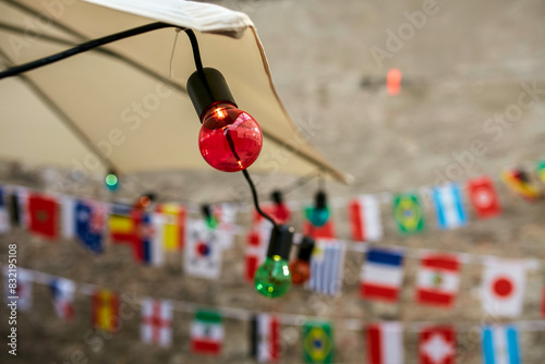 Colored light bulbs are strung in front of a blurred background featuring small international flags hung across a cord. photo
