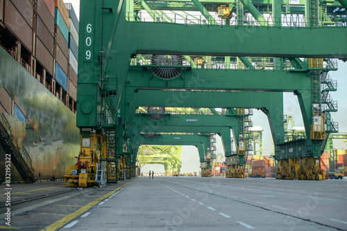 A busy container port with towering green gantry cranes lined up, facilitating the loading and unloading of cargo from a large ship. photo