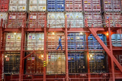 A worker is walking along the narrow gangway of a large cargo ship, surrounded by numerous colorful stacked shipping containers. photo
