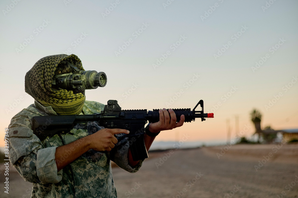 A person in military camouflage attire wearing a gas mask is aiming an assault rifle with a red-dot sight at dusk. A person in military camouflage attire wearing a gas mask is aiming an assault rifle with a red-dot sight at dusk.
