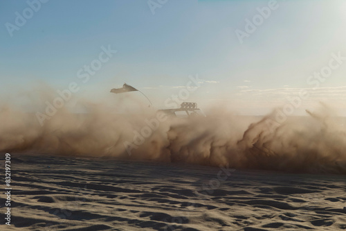 A vehicle speeds across the desert, kicking up a massive cloud of dust in the wake of its passage. photo