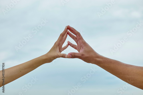 Two hands are forming a triangular shape against a cloudy sky backdrop. photo