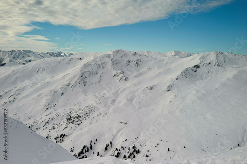A vast snow-covered mountain range under a clear blue sky with shadows indicating the undulations of the terrain.