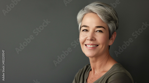 Beautiful mature woman with a glowing smile  her face shining from anti-aging dermatology treatments  on a grey studio background  reflecting her confidence and joy