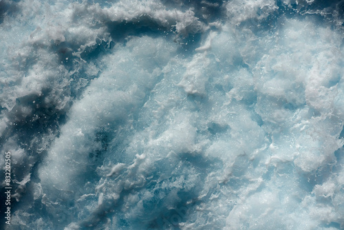 Churning azure waters creating a frothy white texture, showcasing the dynamic movements of the sea. photo