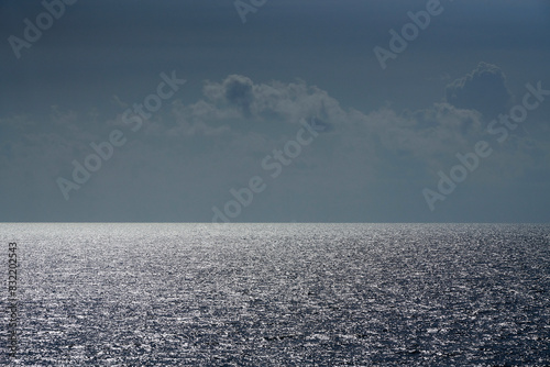 This is an image of a vast ocean under a cloudy sky with sunlight reflecting off the water's surface. photo