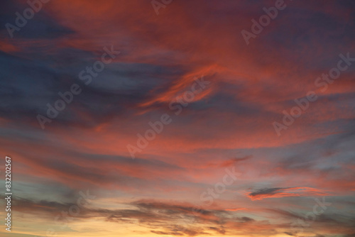 The image captures a vibrant sunset sky with a blend of orange, red, and blue hues, highlighting the dynamic and soft cloud formations. photo