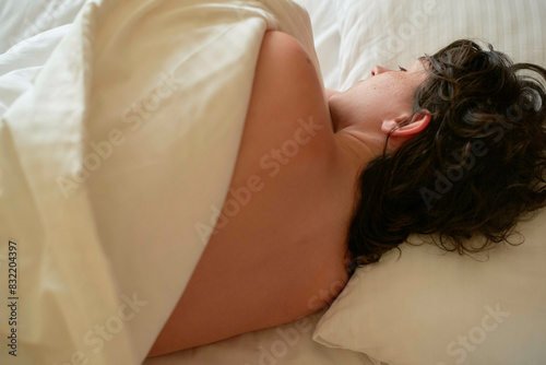A person is lying on a bed with their face turned away, partially covered by a white sheet. photo