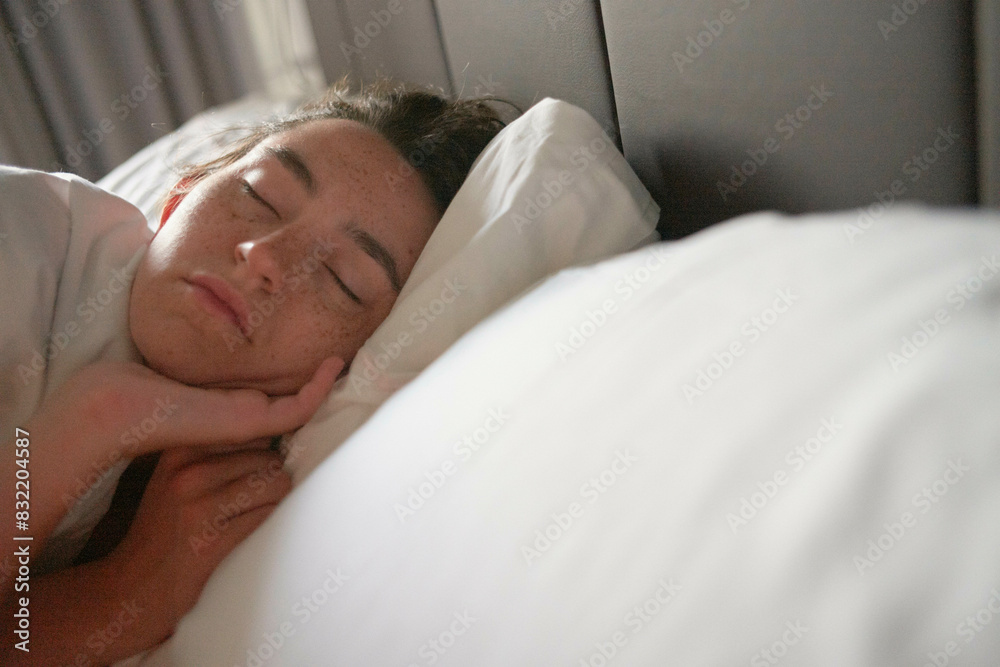 A young woman sleeping peacefully in a bed with white bedding and a subdued lighting environment. A young woman sleeping peacefully in a bed with white bedding and a subdued lighting environment.