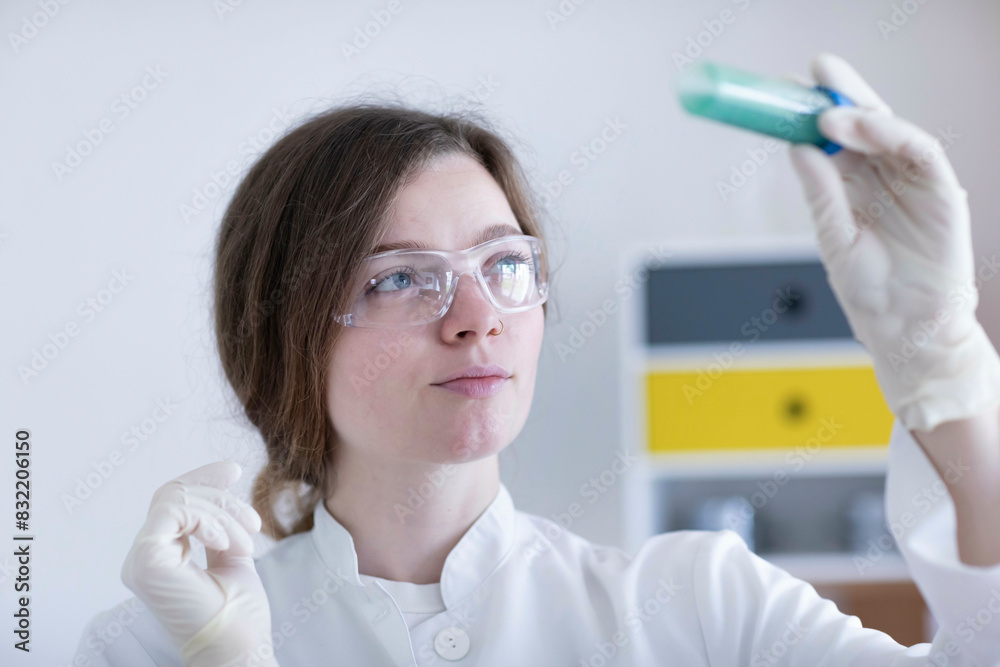 A focused scientist in a lab coat examines the contents of a test tube, wearing safety goggles and gloves. A focused scientist in a lab coat examines the contents of a test tube, wearing safety goggles and gloves.