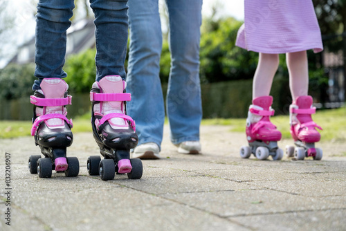 A child and an adult are roller skating together on a paved pathway, with the child wearing pink and black roller skates and the adult in blue denim jeans. photo