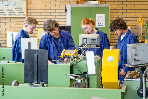 Four people in blue work uniforms are attentively operating and observing machinery in an industrial workshop setting. photo