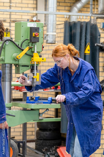 A woman in a blue work coat operates machinery in a workshop, focusing intently on her task. photo