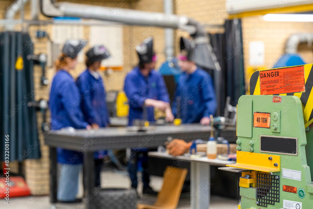 A group of individuals in safety gear are focused on work at a manufacturing workshop, with a prominent green machine in the foreground. A group of individuals in safety gear are focused on work at a manufacturing workshop, with a prominent green machine in the foreground.