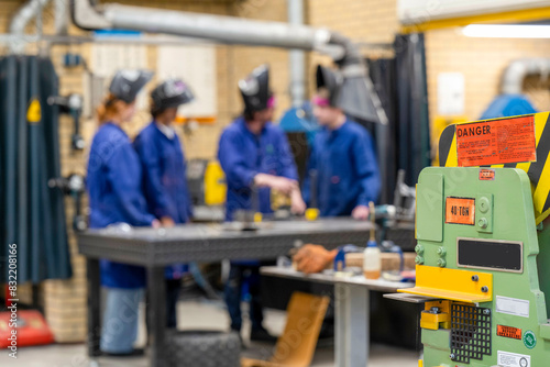 A group of individuals in safety gear are focused on work at a manufacturing workshop, with a prominent green machine in the foreground. photo