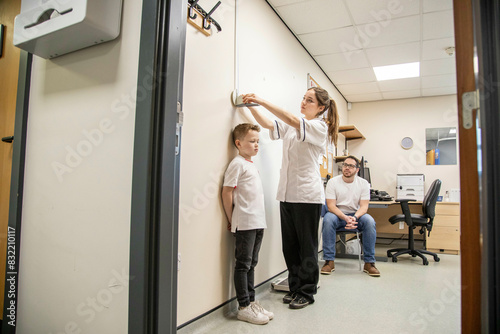 Child being measured during a medical check-up as father observes. photo