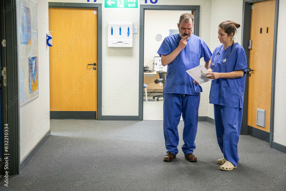 Two healthcare workers consulting in hospital corridor, medical practice UK