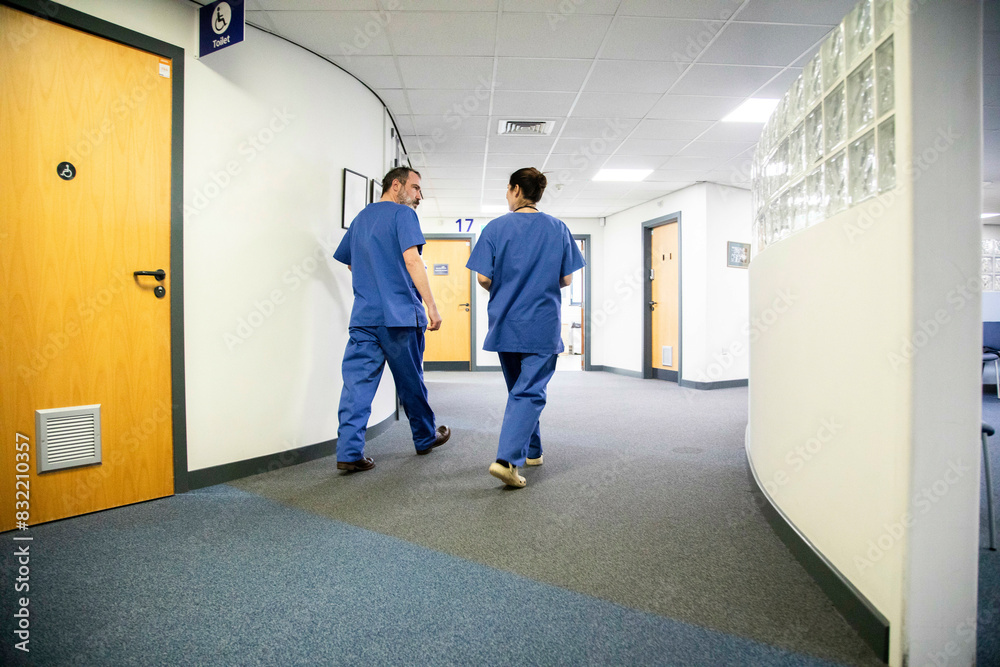 Two healthcare workers walking in a hospital corridor, medical practice UK Two healthcare workers walking in a hospital corridor, medical practice UK