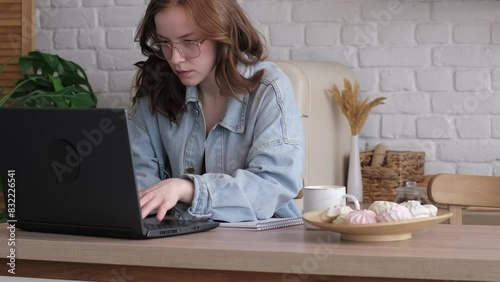 Engrossed in her work, a woman uses her laptop in a bright, minimalist kitchen, highlighting the adaptability required in today's hybrid work models.