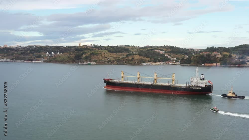 Drone capturing bulk cargo ship moving on seascape by mountains against sky. High angle view of empty bulk carrier on bay during daytime. Drone capturing bulk cargo ship moving on seascape by mountains against sky. High angle view of empty bulk carrier on bay during daytime.