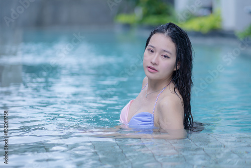 Beautiful young Asian woman in a pink and blue color bikini relaxing in a swimming pool feeling fresh and cooling on vacation holiday.