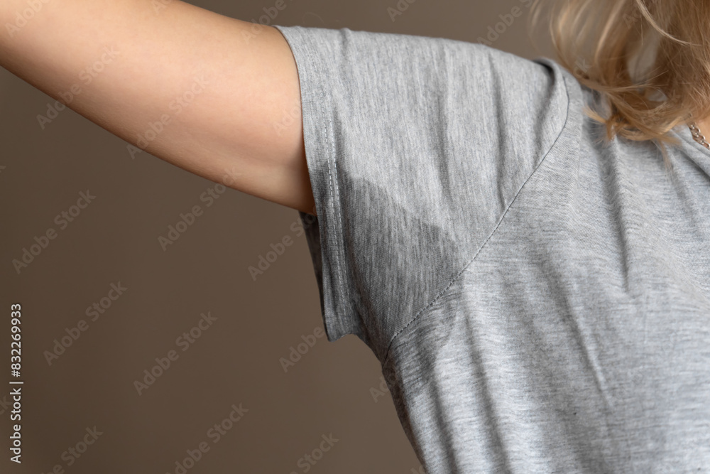 Close-up of a young woman shows a wet armpit on a gray T-shirt. Concept of health, sports