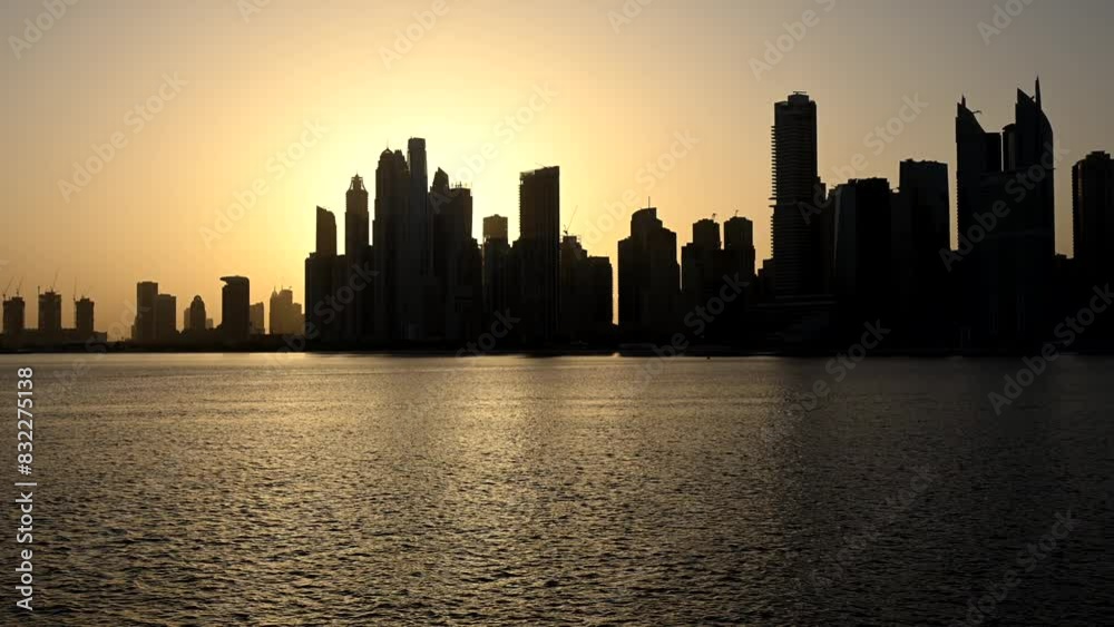 A sprawling cityscape stands against a vast body of water while the sun rises in Dubai, United Arab Emirates A sprawling cityscape stands against a vast body of water while the sun rises in Dubai, United Arab Emirates