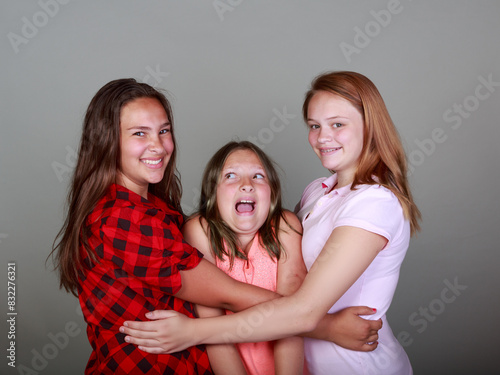 Three girls hug each other, one of them wearing a red plaid shirt