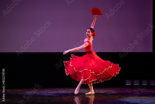 ballerina in a red dress performs a variation from the ballet Don Quixote on the theater stage.