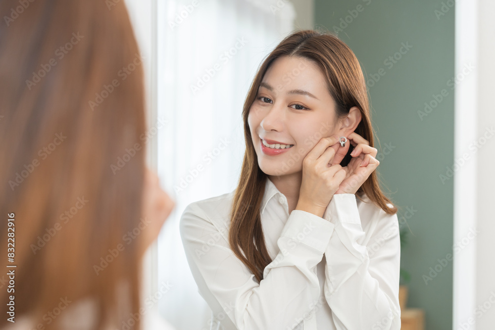 Get dress, pretty asian young woman, businesswoman standing putting earring or jewelry, wearing white shirt formal getting dressed getting ready before go to work looking reflection the mirror at home Get dress, pretty asian young woman, businesswoman standing putting earring or jewelry, wearing white shirt formal getting dressed getting ready before go to work looking reflection the mirror at home