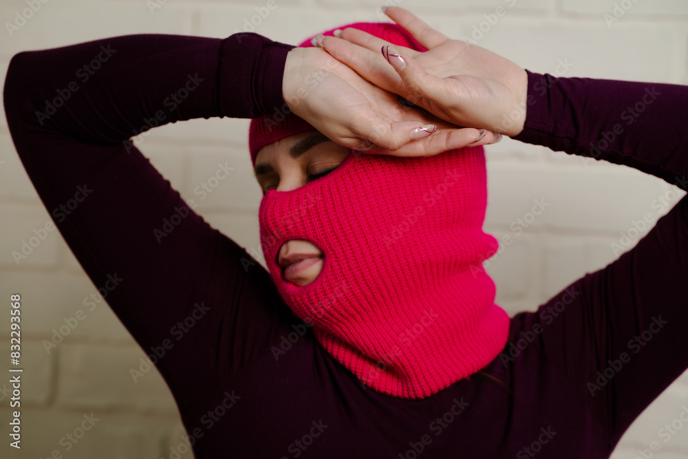 A woman wearing a bright pink balaclava dances energetically, striking unique poses with her hands against a clean, white brick wall background A woman wearing a bright pink balaclava dances energetically, striking unique poses with her hands against a clean, white brick wall background