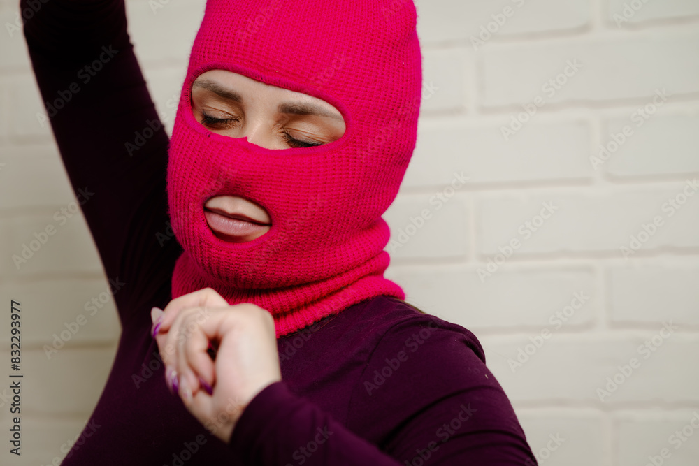 A woman wearing a bright pink balaclava dances energetically, striking unique poses with her hands against a clean, white brick wall background A woman wearing a bright pink balaclava dances energetically, striking unique poses with her hands against a clean, white brick wall background