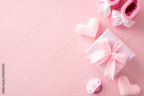 Pastel pink baby shower concept with gift box, knitted hearts, baby booties, and pacifier on pink background