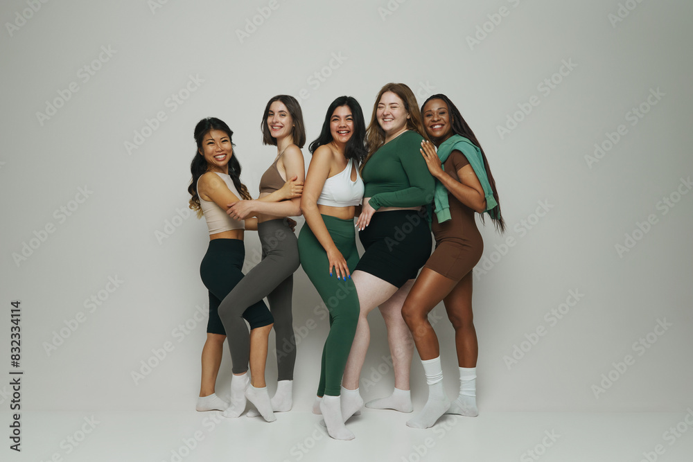 Naklejka premium Portrait of women of different ethnicities and body types pose in fashionable activewear against white studio background. Concept of beauty and fashion, support, unity, wellness, body positivity.