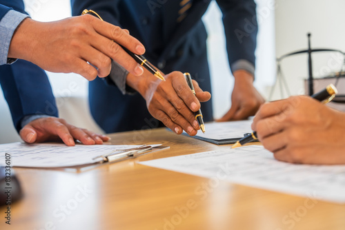 A team meeting of business people and a lawyer in formal suits is taking place at a desk, discussing a contract and various aspects of the law and litigation.