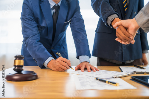 A team meeting of business people and a lawyer in formal suits is taking place at a desk, discussing a contract and various aspects of the law and litigation.