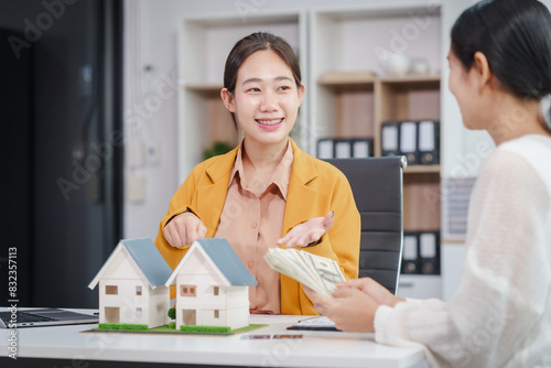 Asian businesswoman discusses home purchase contracts with clients at her desk, focusing on loans, mortgages, and other financial aspects of real estate transactions.