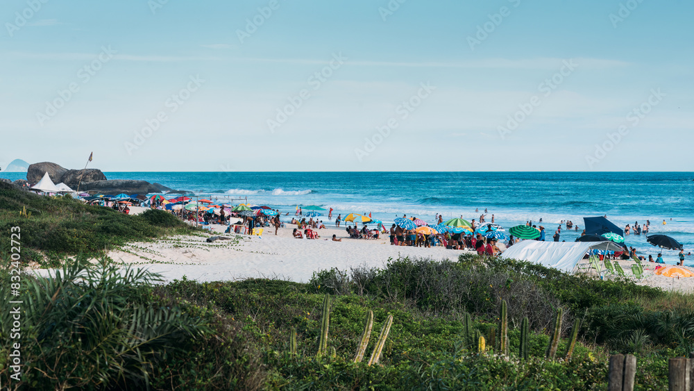 Crowds of beachgoers relax under colorful umbrellas on a sandy shoreline, taking in the ocean views and summer atmosphere, Grumari beach, Rio de Janeiro, Brazil, South America Crowds of beachgoers relax under colorful umbrellas on a sandy shoreline, taking in the ocean views and summer atmosphere, Grumari beach, Rio de Janeiro, Brazil, South America