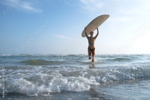 Photography Female surfer wearing a swimsuit holding a surfboard on her head, entering out o