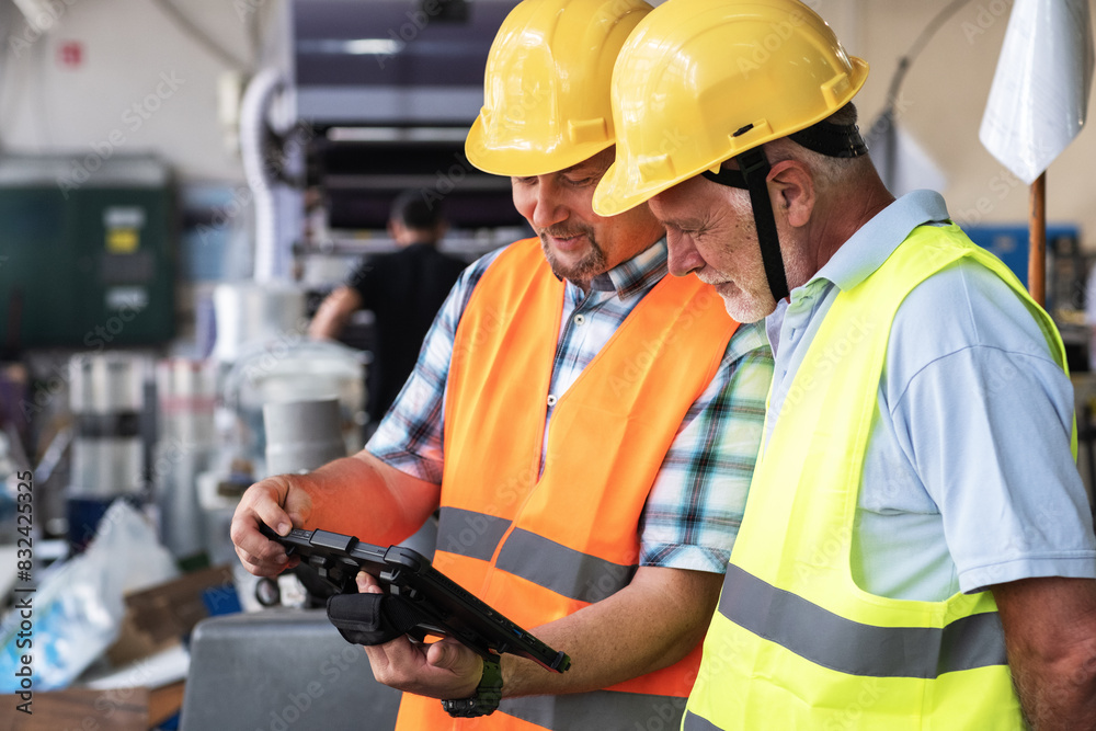 A supervisor stands confidently with a worker on the factory line, using a tablet to check the numbers and quality of production.