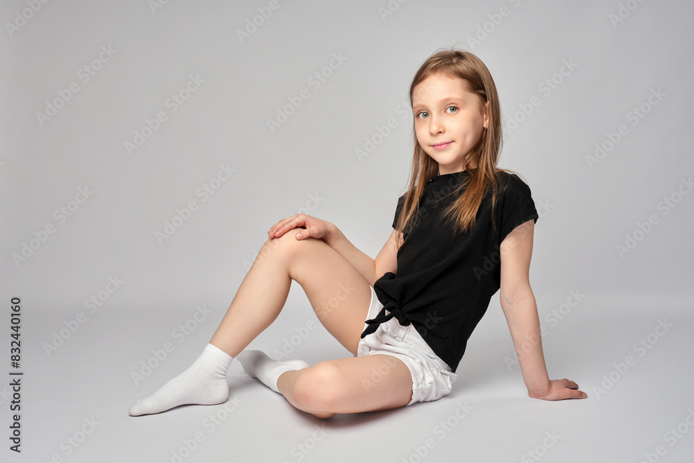 Full length portrait of a cute girl, wearing white shorts and black shirt, sitting on white background Full length portrait of a cute girl, wearing white shorts and black shirt, sitting on white background