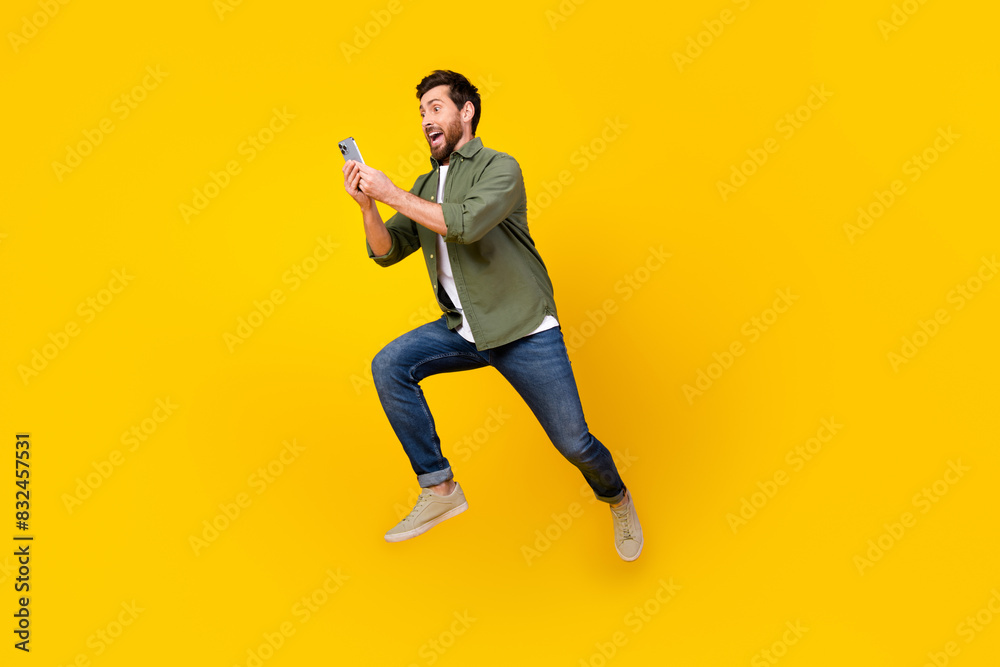 Full size photo of nice young man jump run phone wear shirt isolated on yellow color background Full size photo of nice young man jump run phone wear shirt isolated on yellow color background